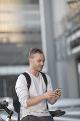 Blond man on bicycle using smart phone - ZEF004505