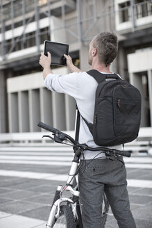 Mann mit Rucksack und Fahrrad beim Fotografieren mit digitalem Tablet - ZEF004506