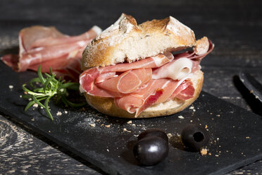 Parmaschinken, Brötchen und schwarze Oliven auf dunklem Holz - MAEF009795