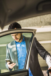 Young businessman with cell phone getting into car - UUF003412