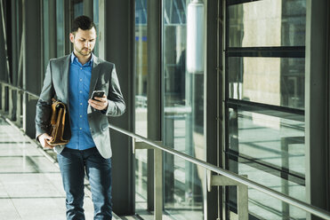 Young businessman walking looking on cell phone - UUF003419