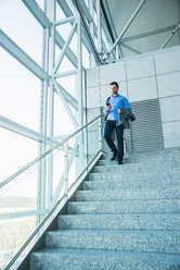 Junger Geschäftsmann geht auf einer Treppe und schaut auf sein Handy - UUF003424