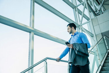 Young businessman with cell phone looking out of window - UUF003455