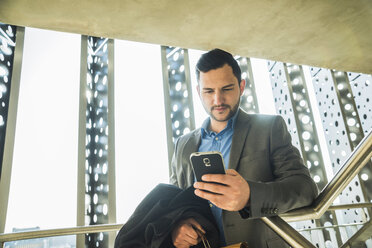 Junger Geschäftsmann auf der Treppe schaut auf sein Handy - UU003459