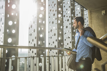 Young businessman with digital tablet looking out of window - UU003435