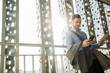 Young businessman holding cell phone and digital tablet - UU003437