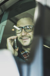 Lächelnder junger Geschäftsmann, der im Auto mit seinem Handy telefoniert - UUF003438