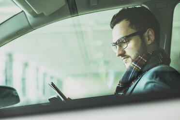 Young businessman in car looking at digital tablet - UUF003441