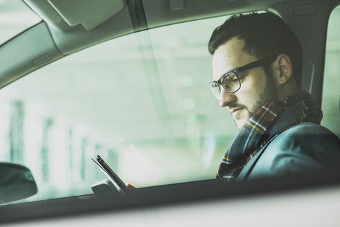 Junger Geschäftsmann im Auto mit Blick auf ein digitales Tablet - UUF003441