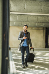 Young businessman walking in car park looking on cell phone - UU003448