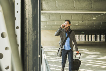 Young businessman walking in car park talking on cell phone - UU003449