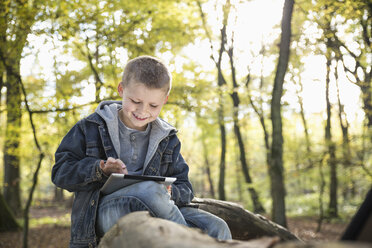 Deutschland, lächelnder kleiner Junge mit digitalem Tablet in einem Wald - PDF000809