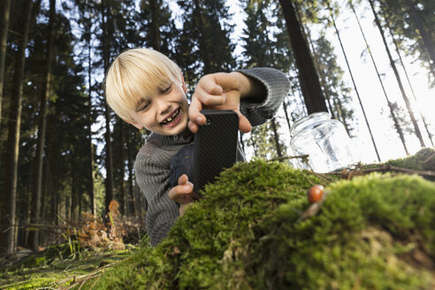 Deutschland, lächelnder kleiner Junge beim Fotografieren der Natur in einem Wald - PDF000822