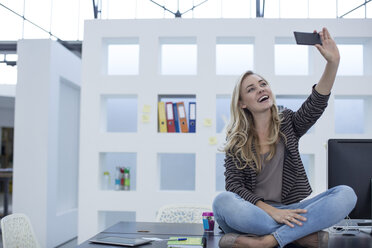 Kreative Bürofrau sitzt auf ihrem Schreibtisch und macht ein Selfie - ZEF003019