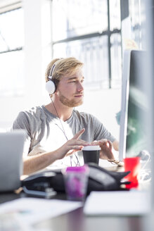 Kreativer Mann im Büro, der an seinem Computer arbeitet und ein Headset trägt - ZEF003088