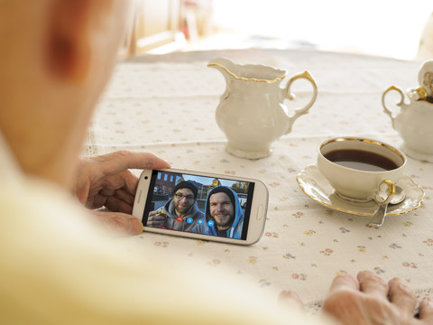 Großvater hält Videokonferenz mit Enkel und Freund via Smartphone, lizenzfreies Stockfoto