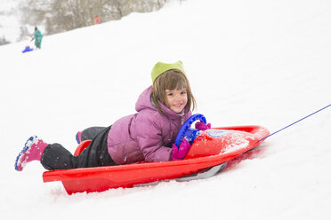 Germany, Swabian mountains, happy little girl lying on sledge - LVF002911