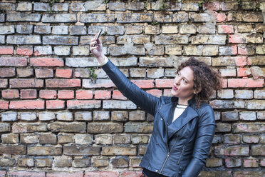 Smiling woman taking selfie in front of brick wall - ANHF000004