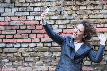 Lächelnde Frau, die ein Selfie vor einer Backsteinmauer macht - ANHF000003