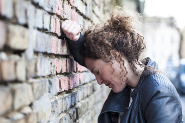 Profil einer Frau mit lockigem braunem Haar, die den Kopf gegen eine Mauer lehnt - ANHF000006