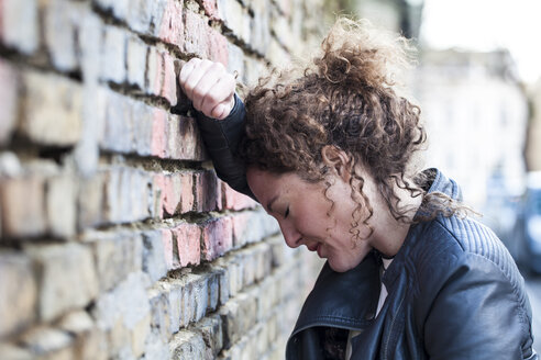 Profile of woman with curly brown hair leaning head against brick wall - ANHF000006