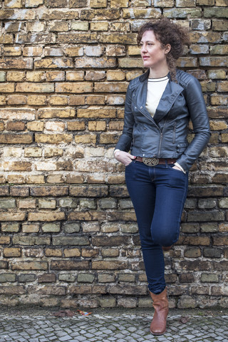 Porträt einer Frau mit lockigem braunem Haar, die sich an eine Backsteinmauer lehnt, lizenzfreies Stockfoto