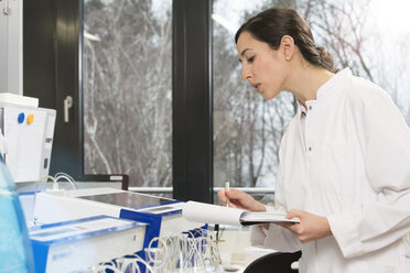 Young scientist noting down results on clip board - FKF000915