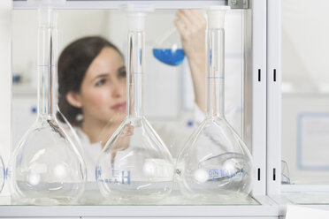 Junge Wissenschaftlerin im Labor, die eine blaue Flüssigkeit in einem Kolben beurteilt - FKF000922
