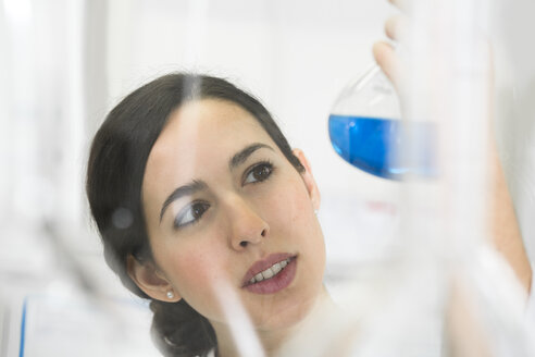 Junge Wissenschaftlerin im Labor, die eine blaue Flüssigkeit in einem Kolben beurteilt - FKF000929