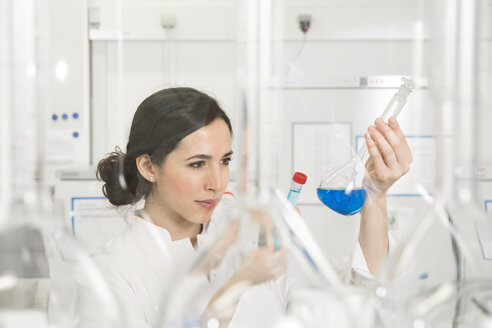 Junge Wissenschaftlerin im Labor, die eine blaue Flüssigkeit in einem Kolben beurteilt - FKF000932