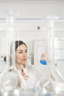 Junge Wissenschaftlerin im Labor, die eine blaue Flüssigkeit in einem Kolben beurteilt - FKF000933