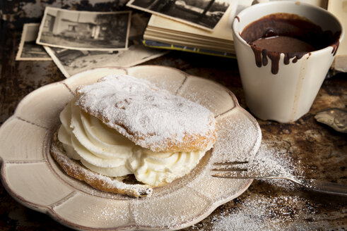 Aufgeschnittenes Brötchen mit Schlagsahne, eine Tasse heiße Schokolade und alte Fotografien - CSTF000870