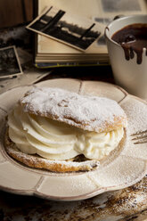 Aufgeschnittenes Brötchen mit Schlagsahne, eine Tasse heiße Schokolade und alte Fotografien - CSTF000871