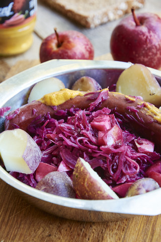 Rotkohl mit Äpfeln, serviert mit roten Pellkartoffeln und einer veganen Wurst, lizenzfreies Stockfoto