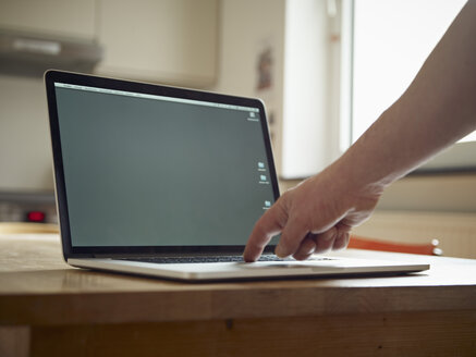 Laptop auf dem Küchentisch, die Hand drückt die Taste - RHF000553