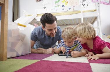 Vater und Kinder benutzen Mini-Tablet, auf dem Boden liegend - RHF000601