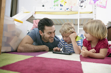 Vater und Kinder benutzen Mini-Tablet, auf dem Boden liegend - RHF000602