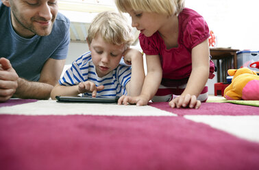 Vater und Kinder benutzen Mini-Tablet, auf dem Boden liegend - RHF000603