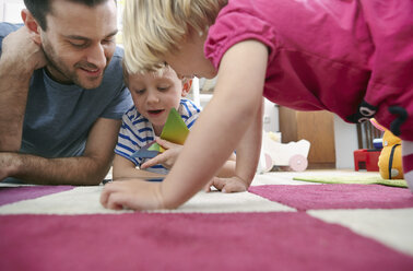 Father and children using mini tablet, lying on floor - RHF000604