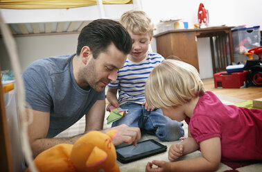 Vater und Kinder benutzen Mini-Tablet, auf dem Boden liegend - RHF000605