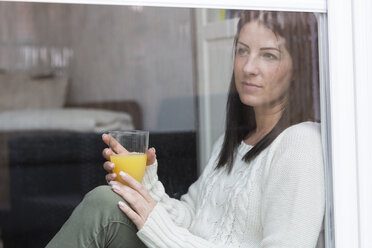 Frau mit Glas Orangensaft schaut durch ein Fenster - SHKF000261