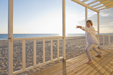 Portugal, Algarve, Frau macht Yoga-Übungen am Strandhaus bei Sonnenuntergang, lizenzfreies Stockfoto