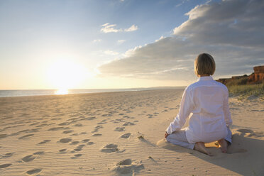 Portugal, Algarve, woman doing yoga exercises at beach house at sunset - MSF004494