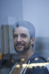 Portrait of smiling man with beard looking through window - RBF002517