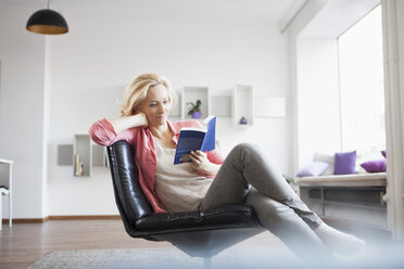 Frau entspannt mit Buch auf Ledersessel zu Hause - RBF002489