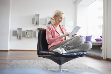 Frau entspannt sich mit digitalem Tablet auf einem Ledersessel zu Hause - RBF002490