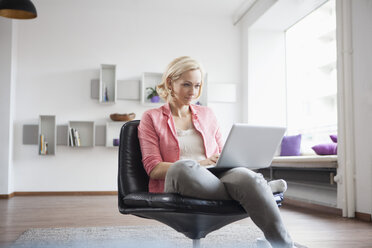 Frau sitzt mit Laptop auf einem Lederstuhl zu Hause - RBF002491