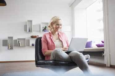 Frau sitzt mit Laptop auf einem Lederstuhl zu Hause - RBF002492