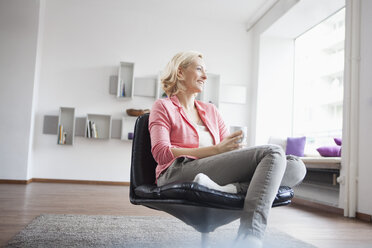 Frau mit Tasse Tee entspannt sich auf einem Ledersessel zu Hause - RBF002495