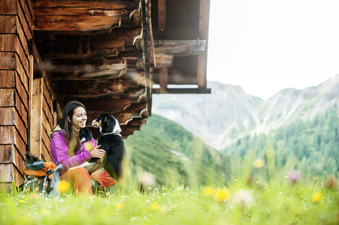 Österreich, Altenmarkt-Zauchensee, junge Frau mit Hund vor einer Alphütte - HHF005114